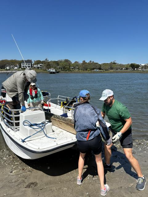 Three people working together to get marine debris onto a boat
