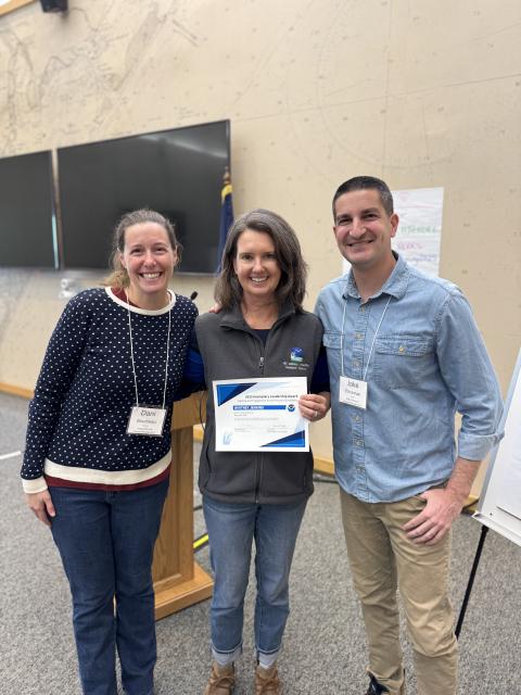 Three smiling people standing up, with Whitney Jenkins in the middle holding her certificate.