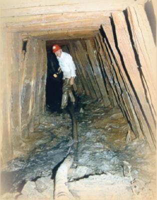 An underground mine shaft with wood supports along the walls and a homeowner standing inside wearing a hard hat