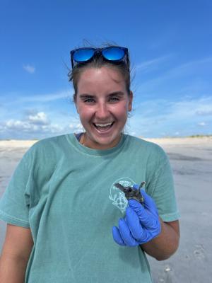 Person smiling and holding a baby sea turtle