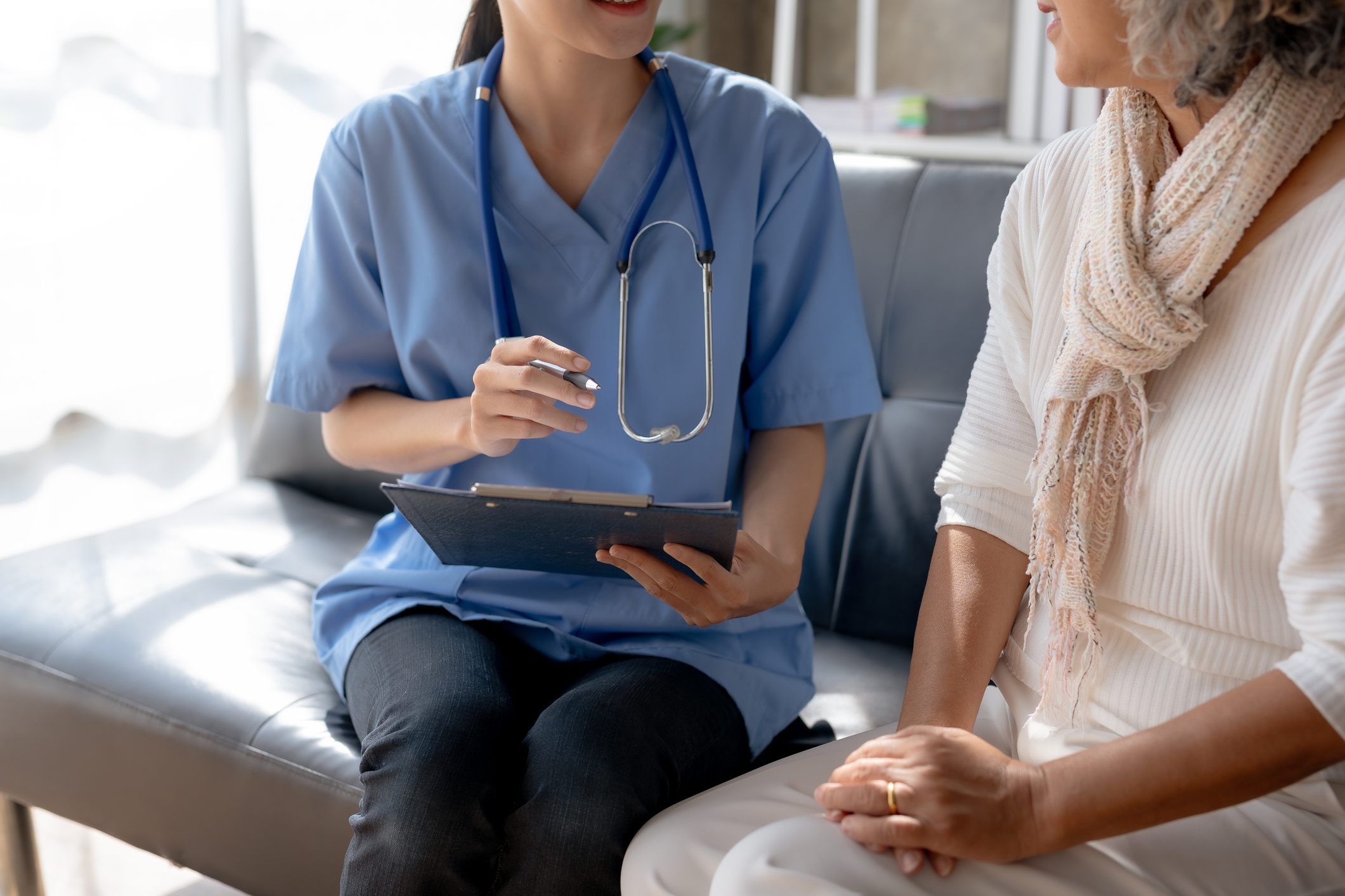 Female nurse sitting with patient in the lobby while holding a clipboard