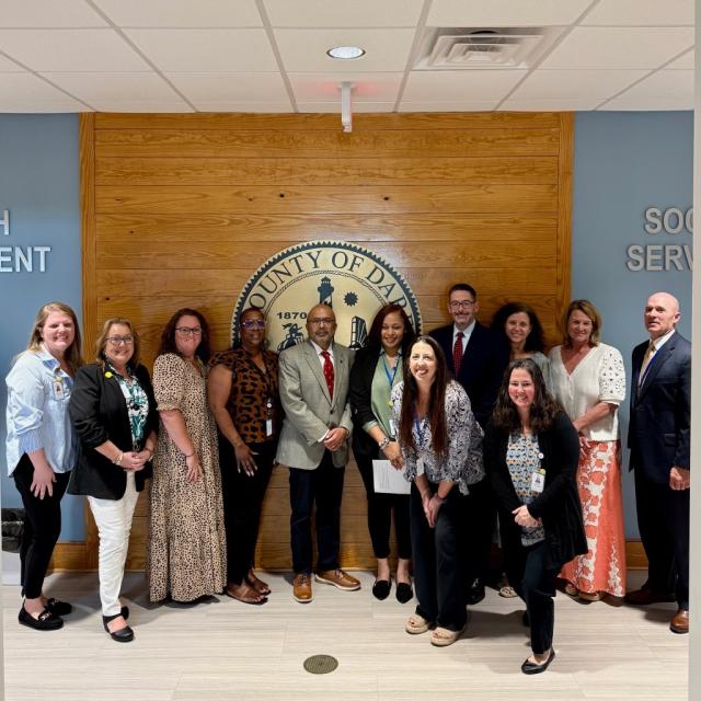 Secretary Sangvai, Deputy Secretary Michael Leighs with Dare County Social Services Staff in front of Dare County's Seal