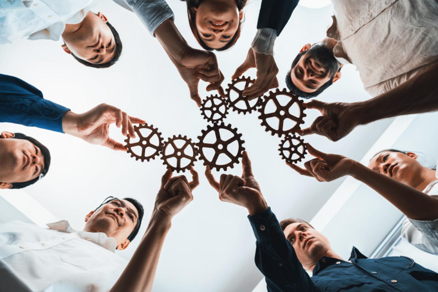 Seven professionals each hold a cog in hand, uniting them as a team process.