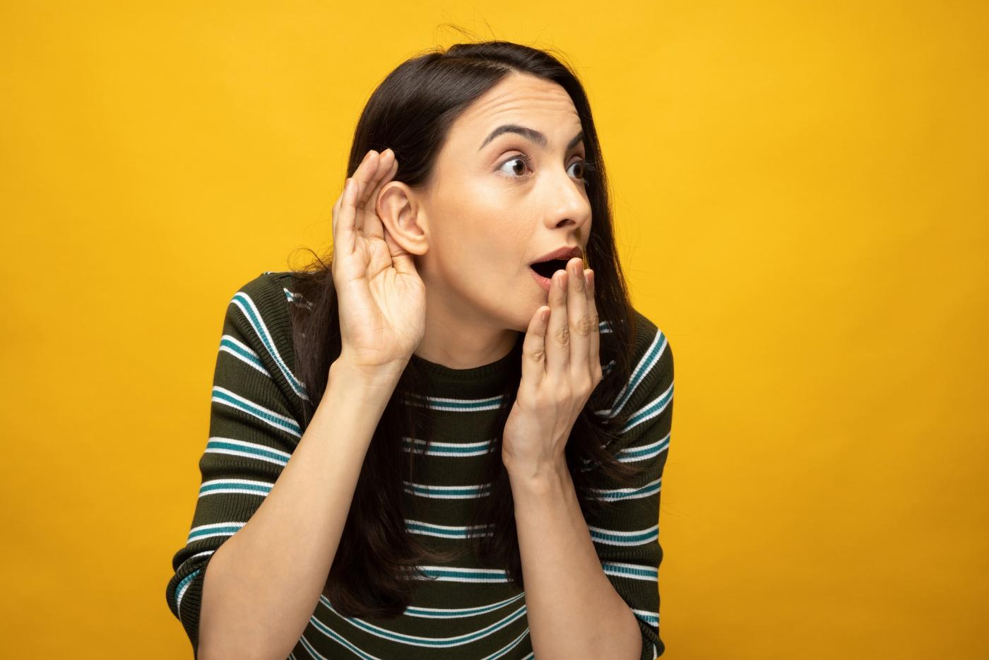 woman holding hand to ear with shocked facial expression