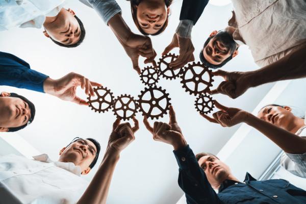 Seven professionals each hold a cog in hand, uniting them as a team process.