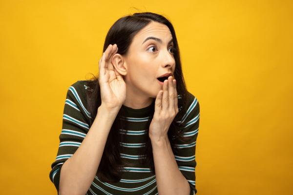 woman holding hand to ear with shocked facial expression