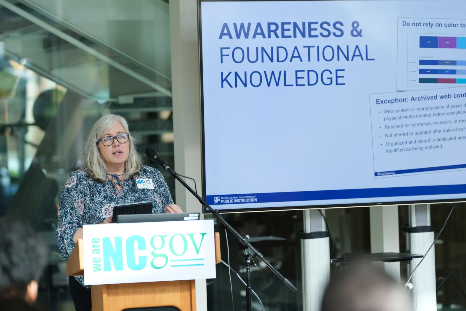A woman speaks behind a podium with a sign for the We Are NC Gov conference..