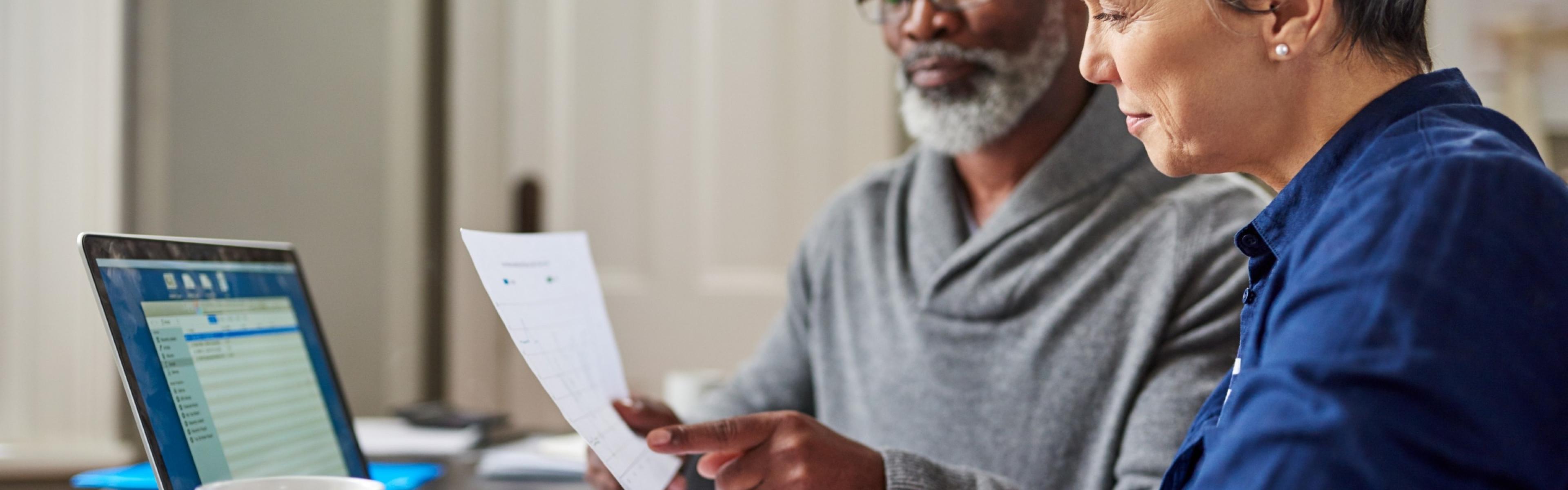 elderly couple working on laptop, finances, and looking at paper