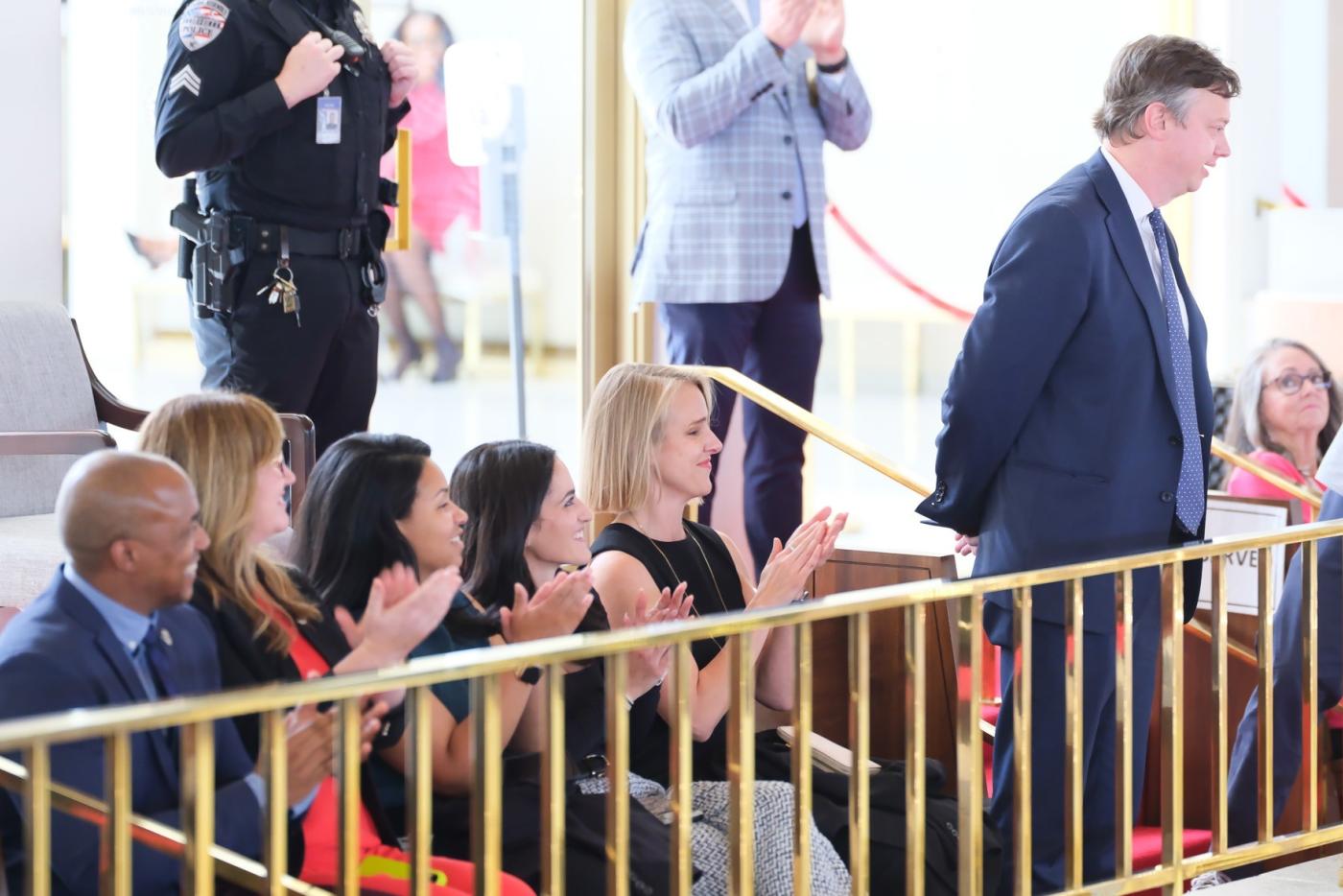 Secretary Nate Denny stands behind a balcony railing as NCDIT leaders smile and clap