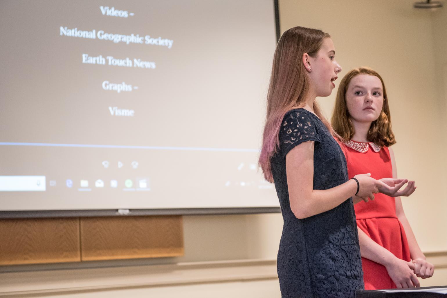 Two NHD students stand in front of a screen showing their documentary project.