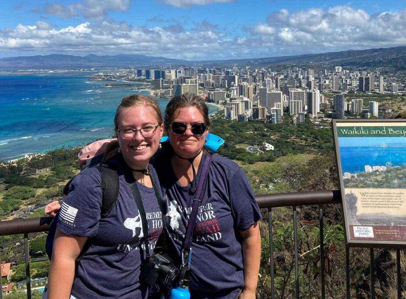 Andi and Amy Bradsher, a NC student and teacher team, pose in front of a coastal Hawaii city skyline.