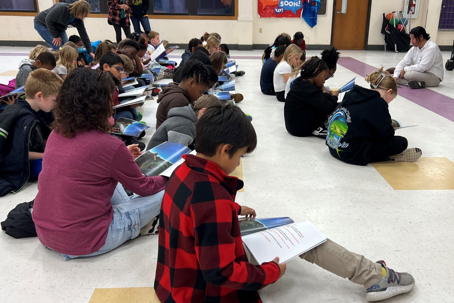 Hugo sits on the floor with a group of elementary students and reads a book.