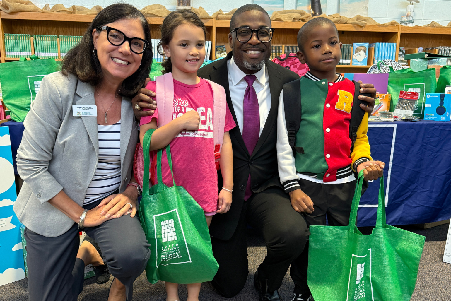 Secretary Cashwell and Superintendent Dr. Lassiter pose with students holding new school supplies.
