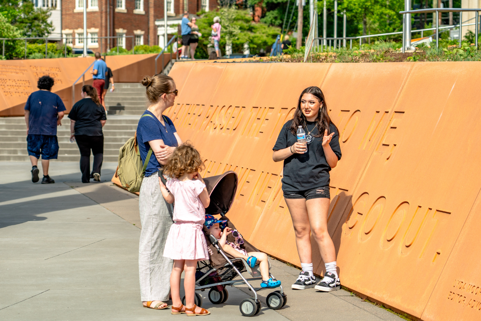 A student talks to a mom with two small children in Freedom Park.