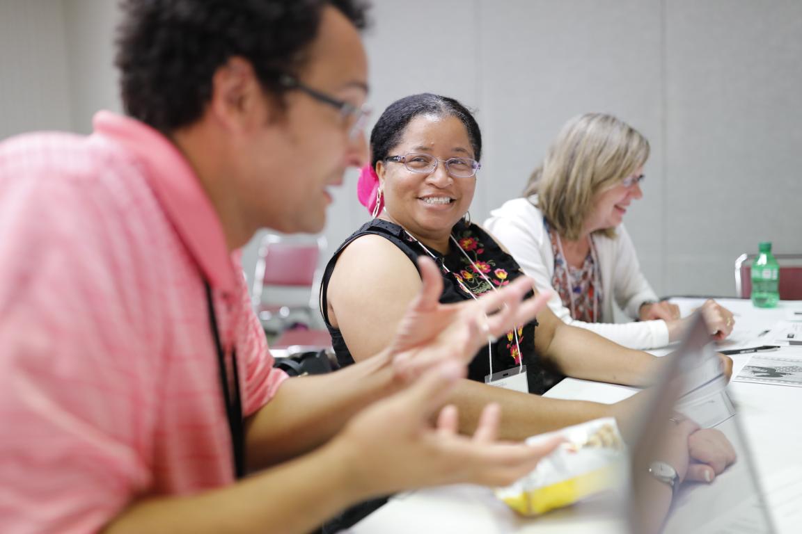 3 teachers sit at a table smiling at a teacher workshop.