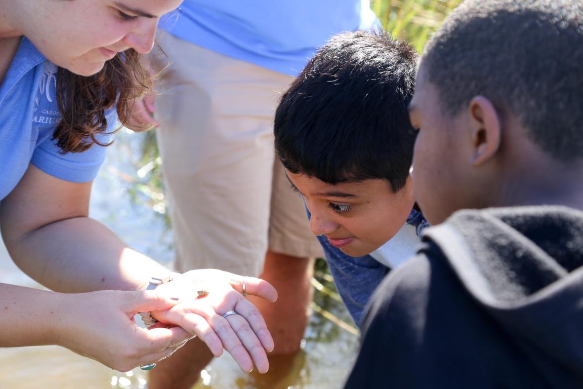 Aquarium staff member shows a snail to two students.