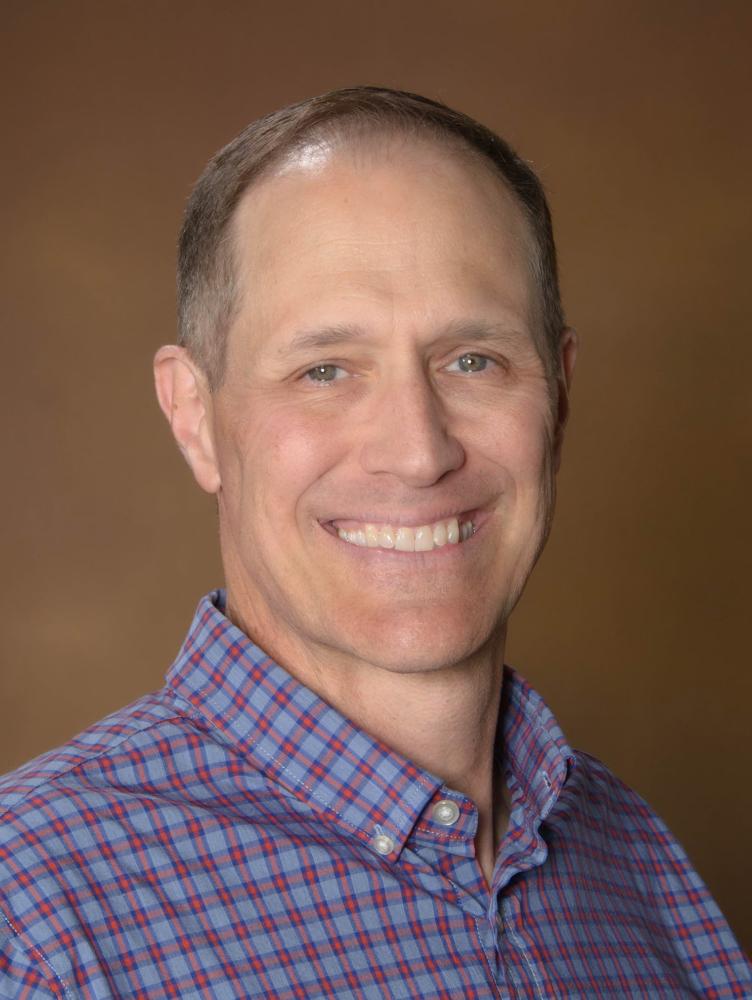 close up of man's face with dark hair, red and blue checkered shirt