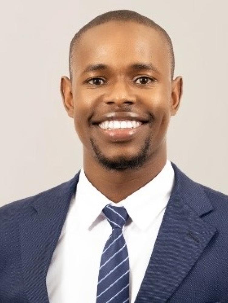 An African American man in a blue suit smiles at the camera. 