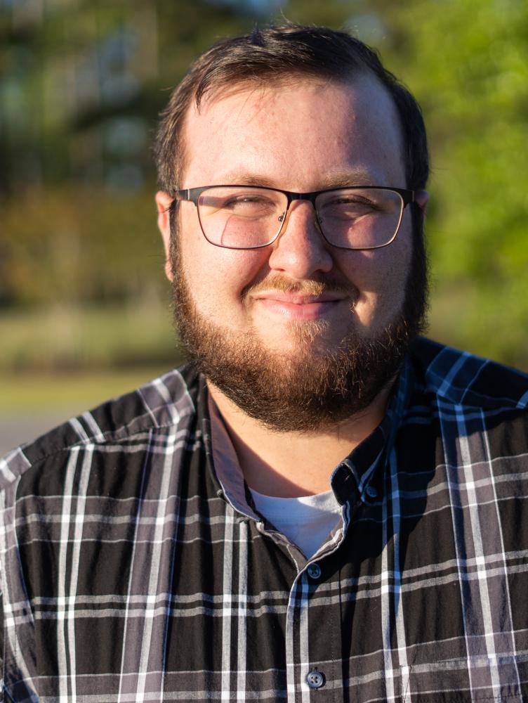 a white man with glasses and a plaid shirt smiles at the camera