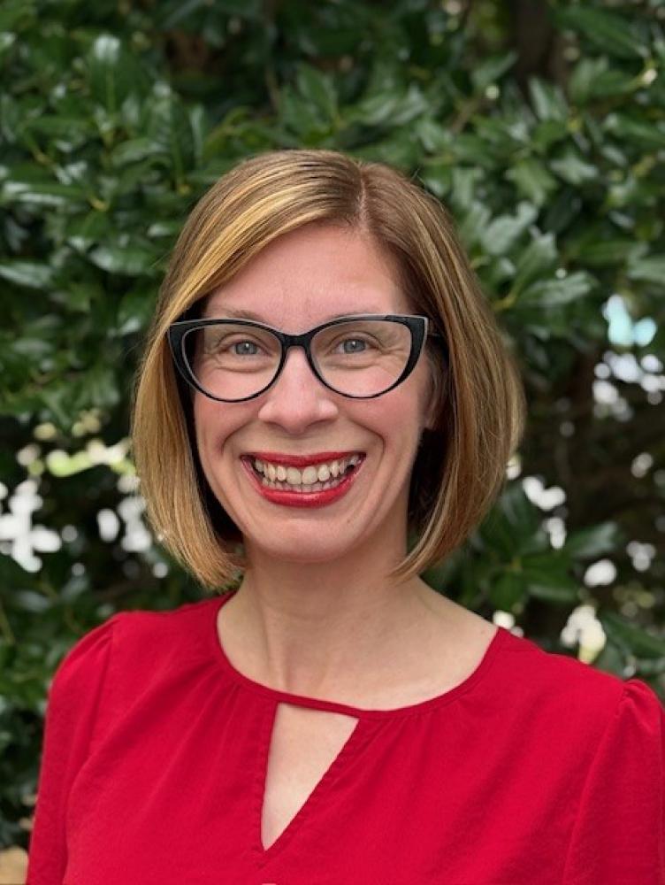 a woman with chin length auburn hair and a red shirt smiles at the camera