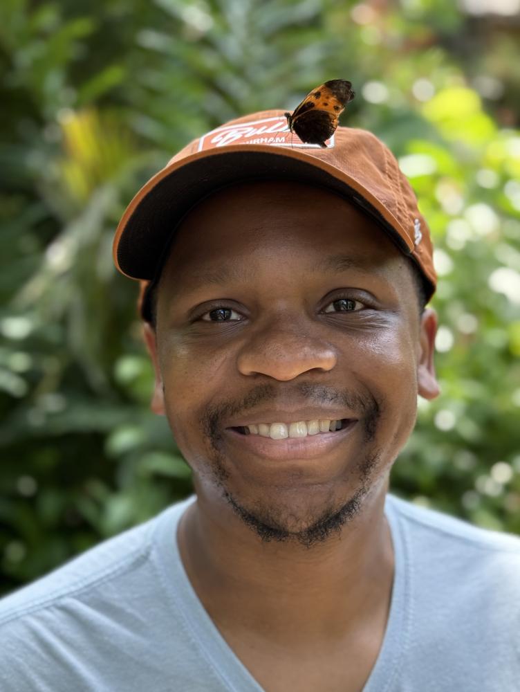 An African American man in a hat smiles as a butterfly perches on his head