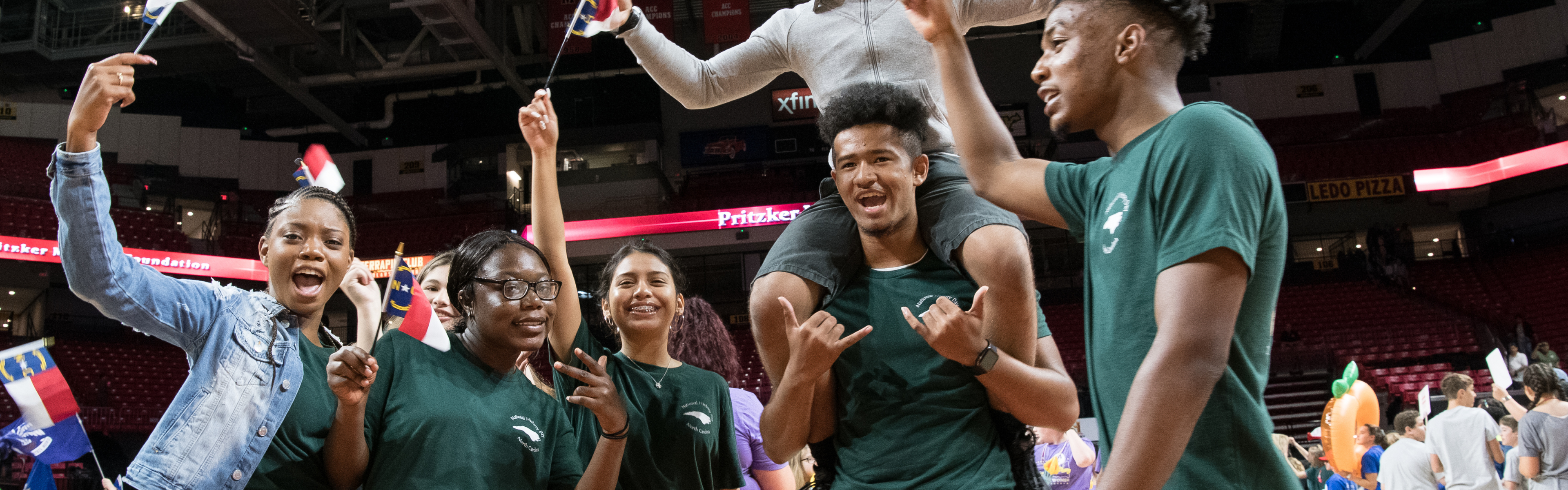 A group of six History Day students smile and wave North Carolina flags at the National Contest.