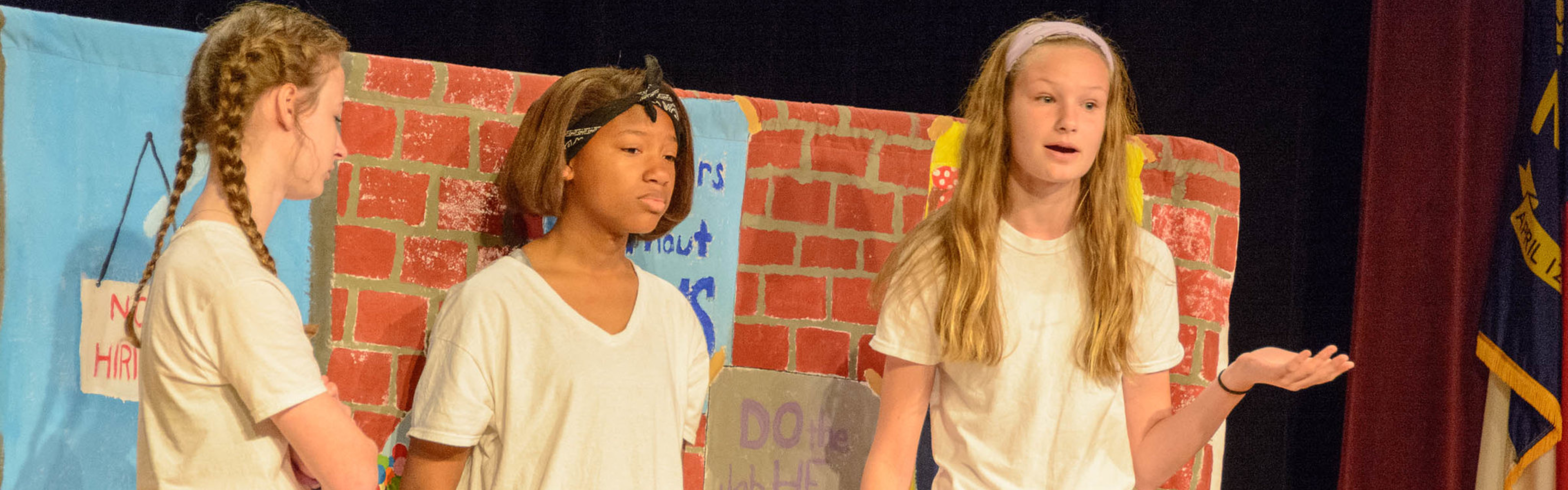 A group of three History Day students present their performance on a stage.