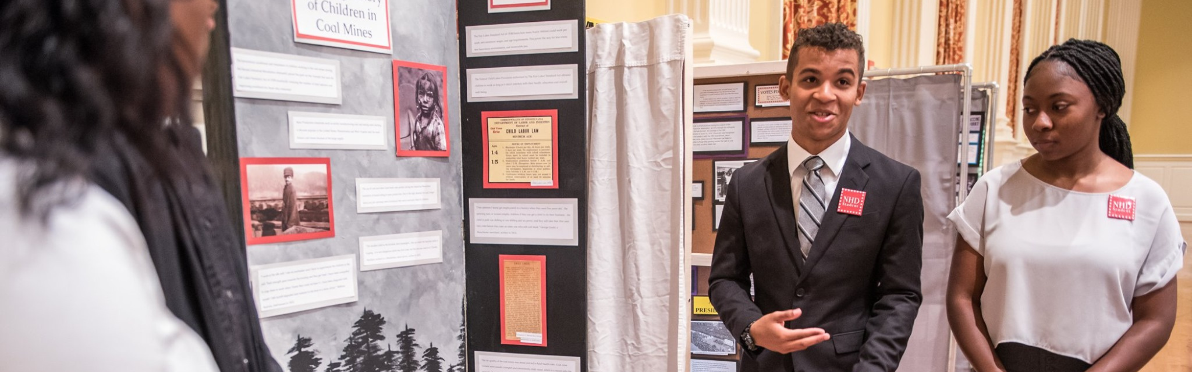 A group of three History Day students stand in front of their exhibit and answer judges interview questions.