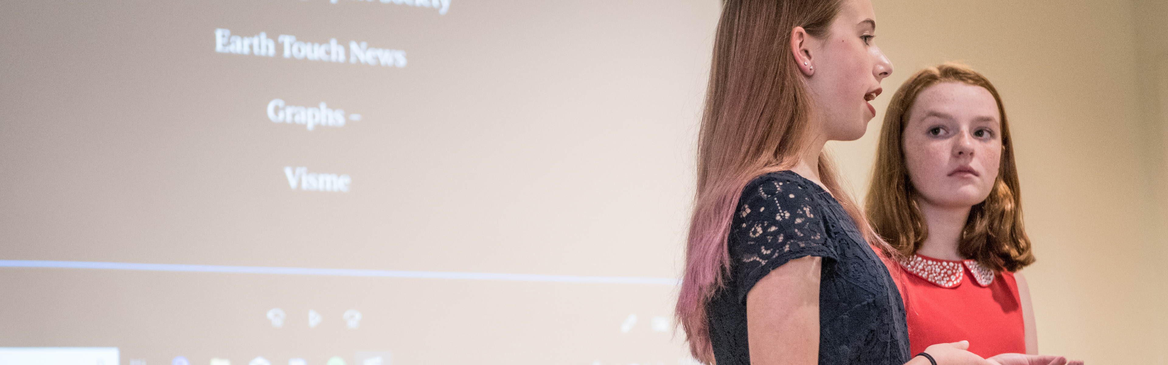 Two History Day documentary students talk to their judges in front of their documentary on a classroom screen.