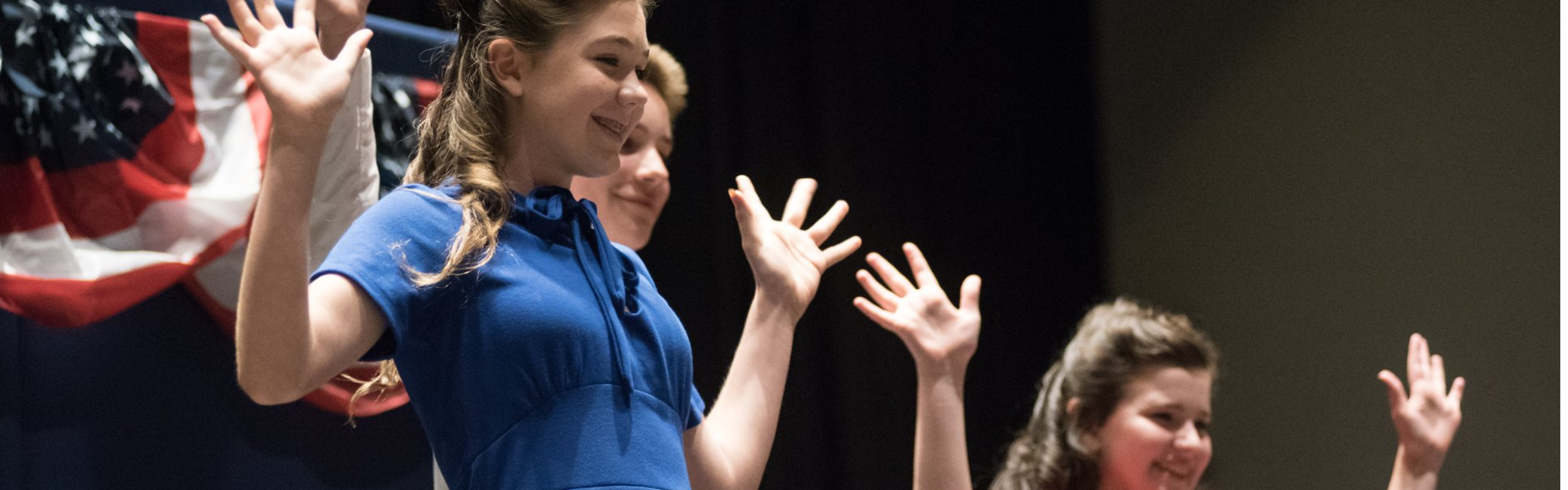 A group of three History Day students dance during their performance on a stage.