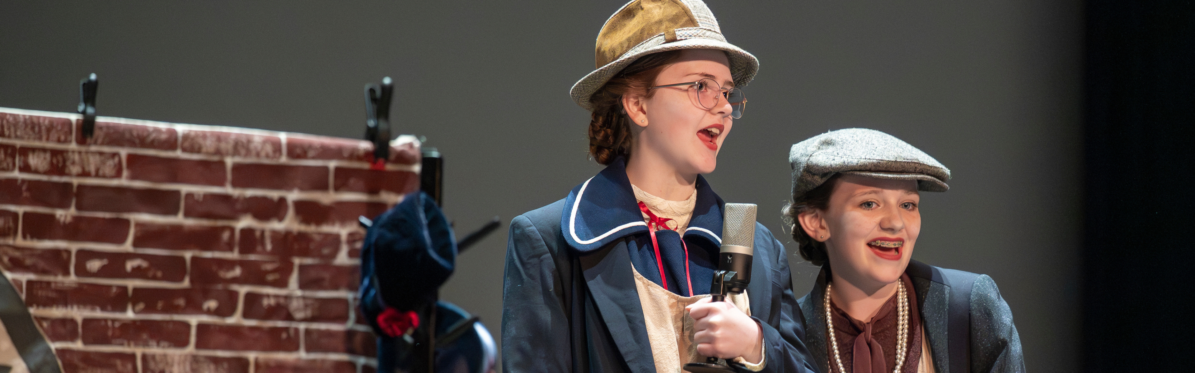 Two students perform on stage in historic costumes.