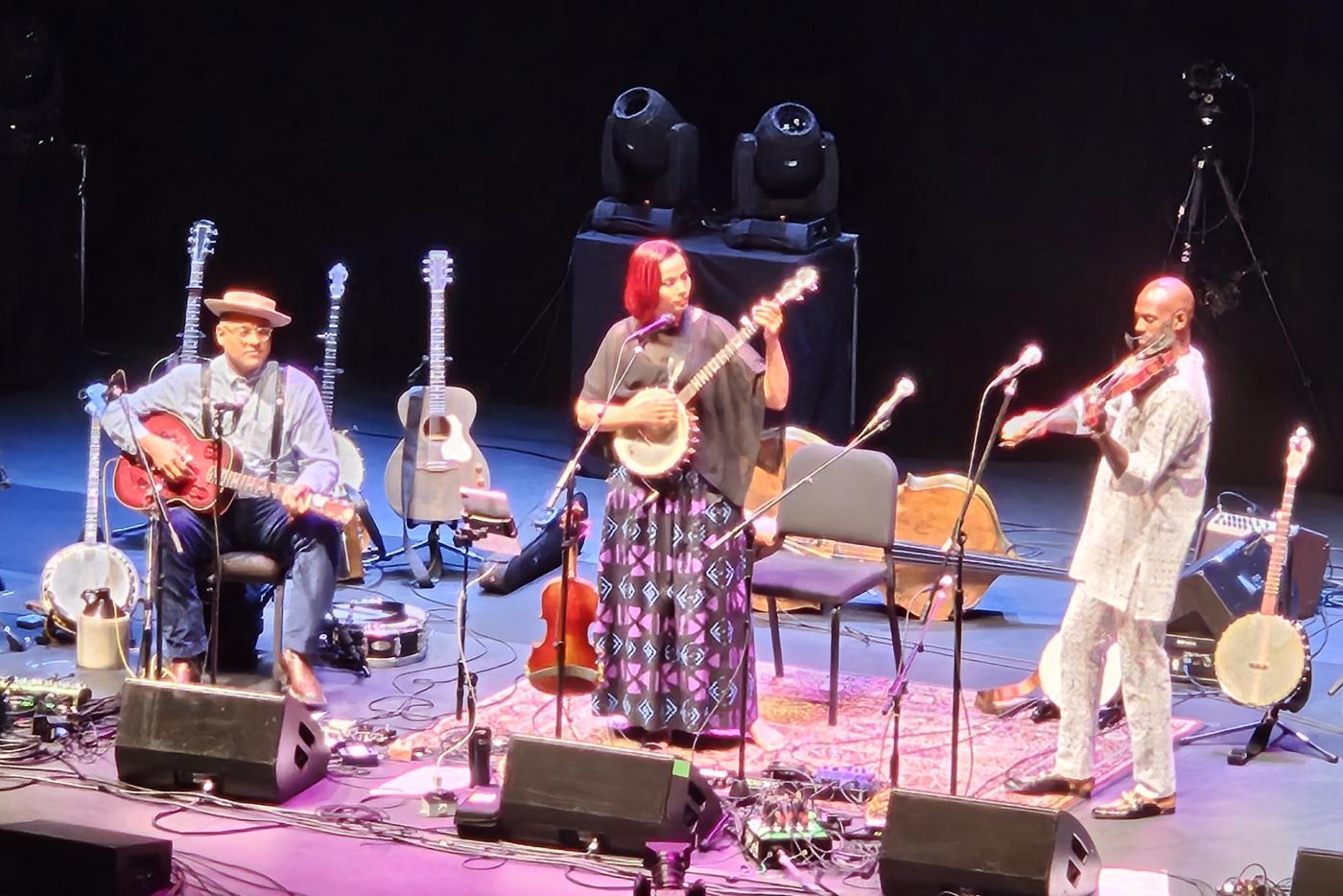Three Musicians Play on Stage with a guitar, banjo, and fiddle.
