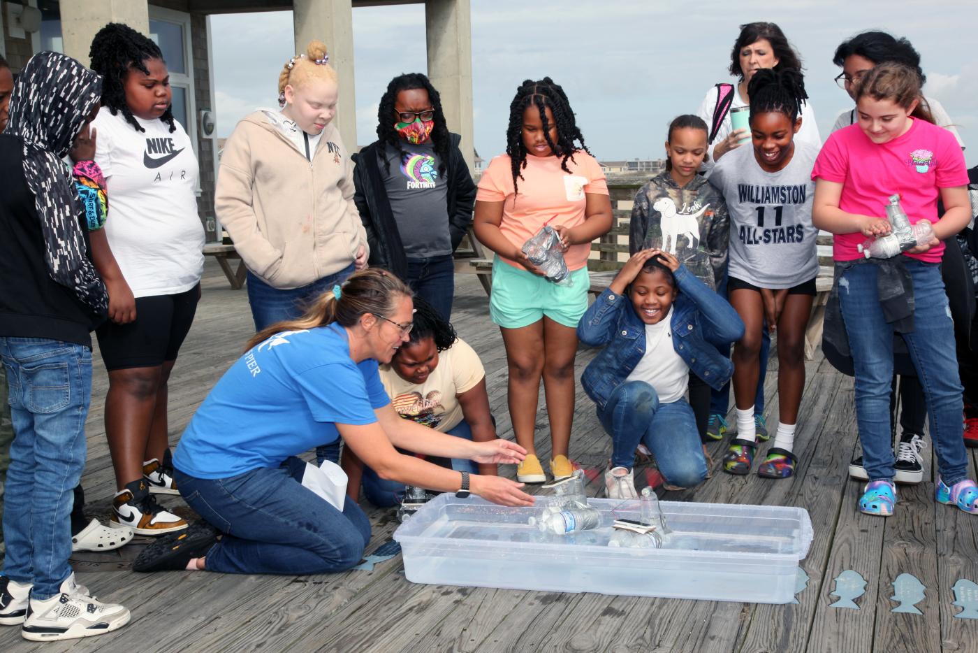 An aquarium educator sits on the pier and leads a demonstration for students.