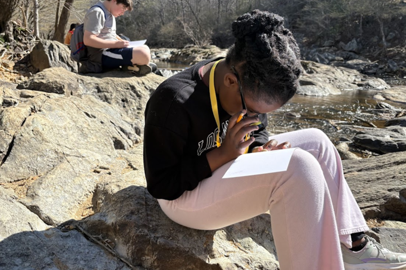 student using magnifying glass by a rocky river