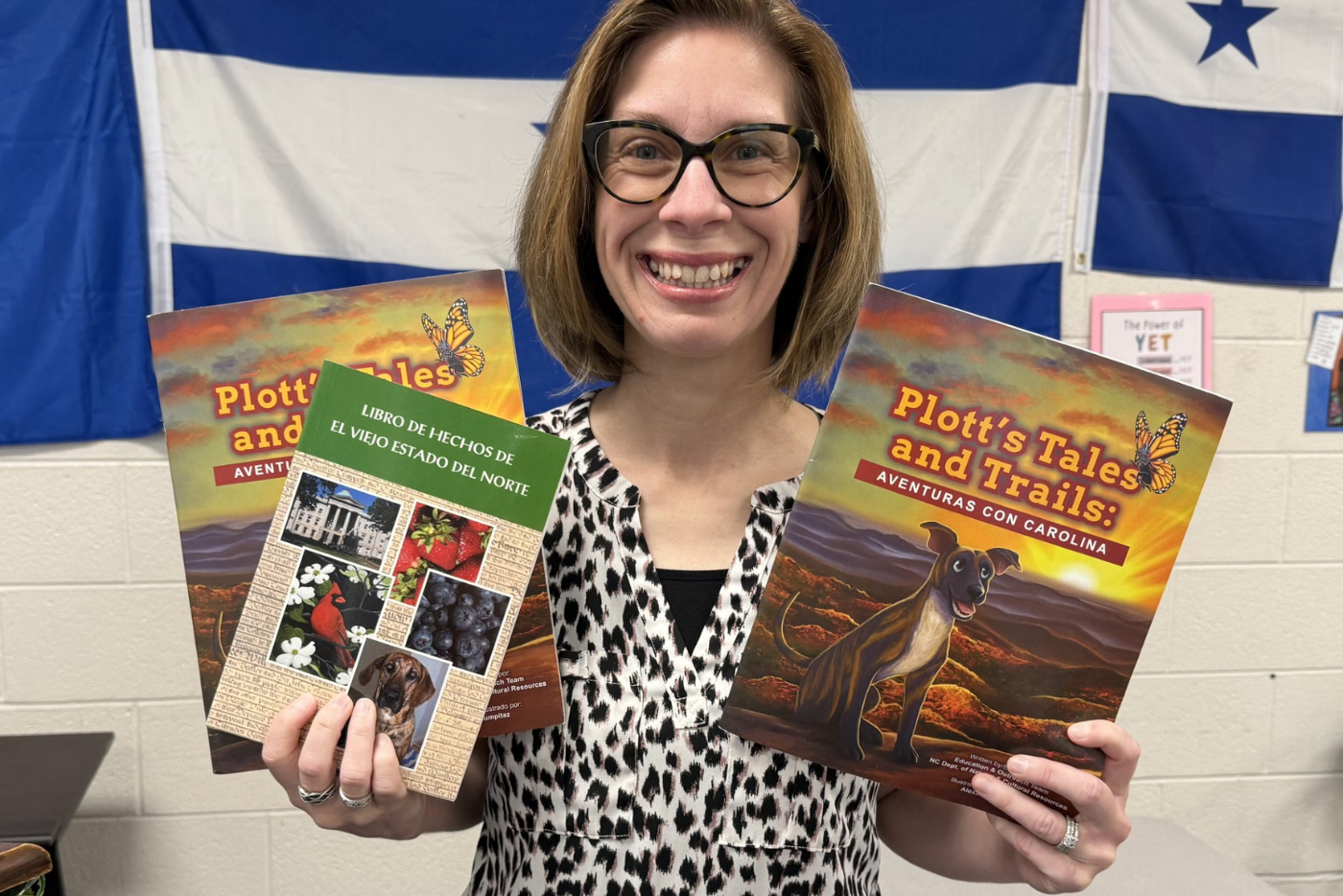Teacher smiles and holds up copies of Plott's Tales and Trails Book