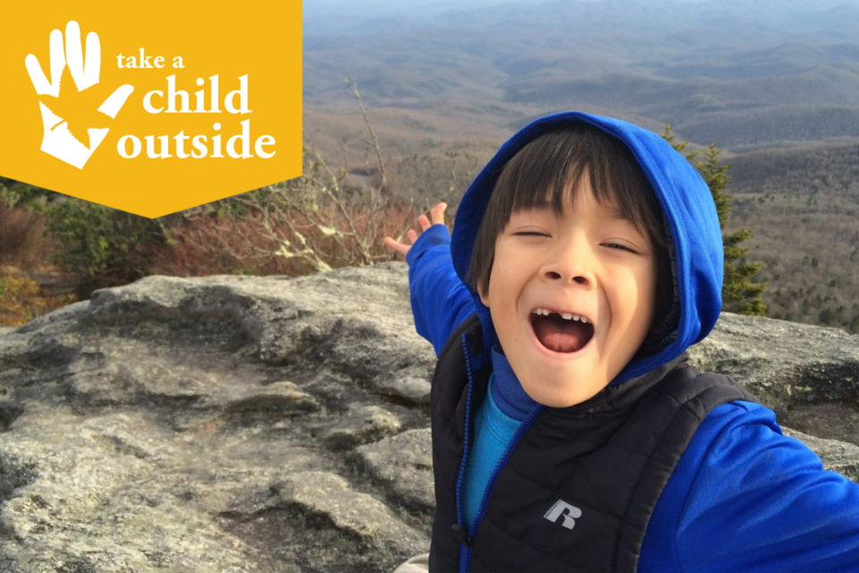 A young boy smiles at the camera at the top of a mountain.