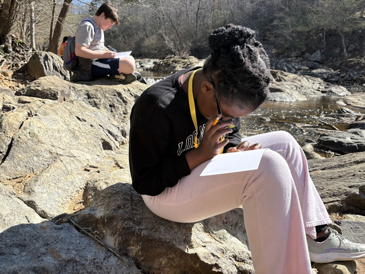 student using magnifying glass by a rocky river