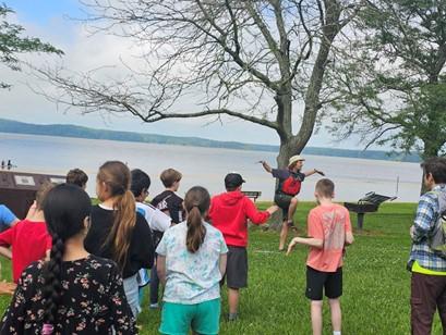 A park ranger leads a group of students in poses of animals outside.