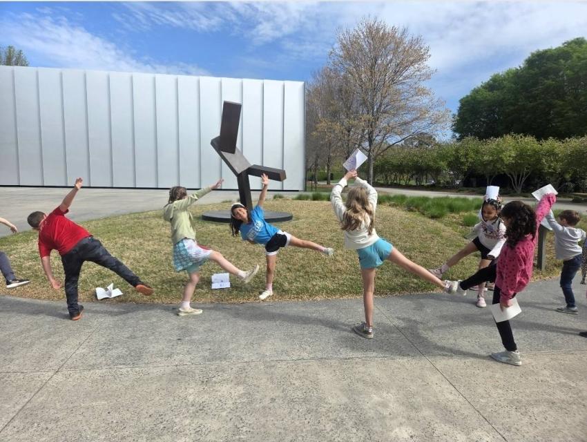 a group of students imitate the poses of a sculpture outside the NC Museum of Art.