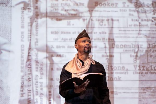 Dr. Sonny Kelly stands on stage while wearing a uniform and holding a book open.