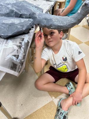 a student sits on the floor and paints a paper mache elephant