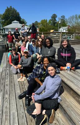 A group of people sit on on a dock and smile at the camera