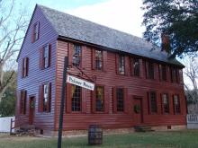 A red two-story clapboard sided building with sign stating "Palmer House" and a white picket fence