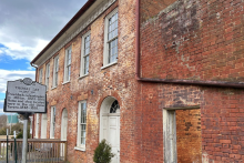 A brick tavern with eight windows and two doors, and historic marker discussing Thomas Day