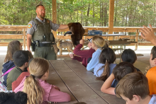 A park ranger holds an animal pellet in front of elementary school students