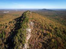 An aerial shot of a sharp ridgeline of Crowders Mountain, and a mountain peak in the distance