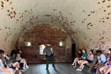 A park ranger points to a curved brick ceiling of a fort, teaching students about architecture