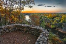 A semi-circle rock wall overlook post above an autumnal forest and rive