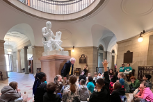 Students sit below a statue of a Roman-styled George Washington and a tour guide. A open balcony is in the ceiling.