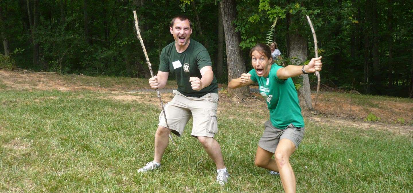 Two happy teachers hold up sticks as if playing.